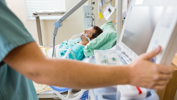 Image of RT working on a monitoring machine at the bedside of a hospital patient