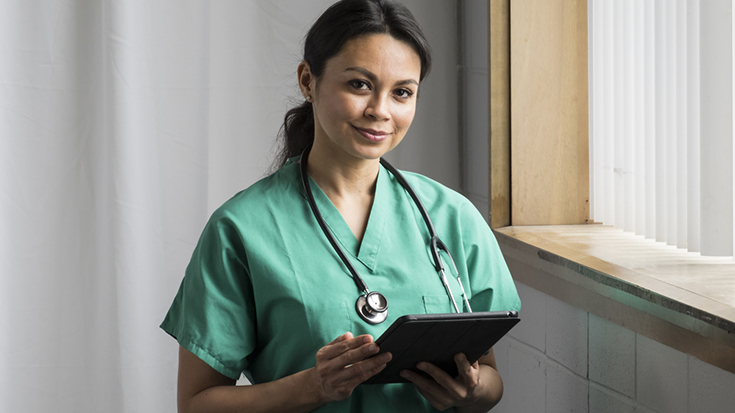 woman medical provider wearing scrubs, holding tablet