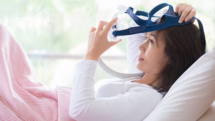 image of woman putting on CPAP mask
