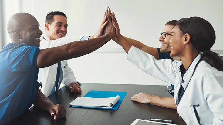 image of group of medical professionals at table giving each other a high five