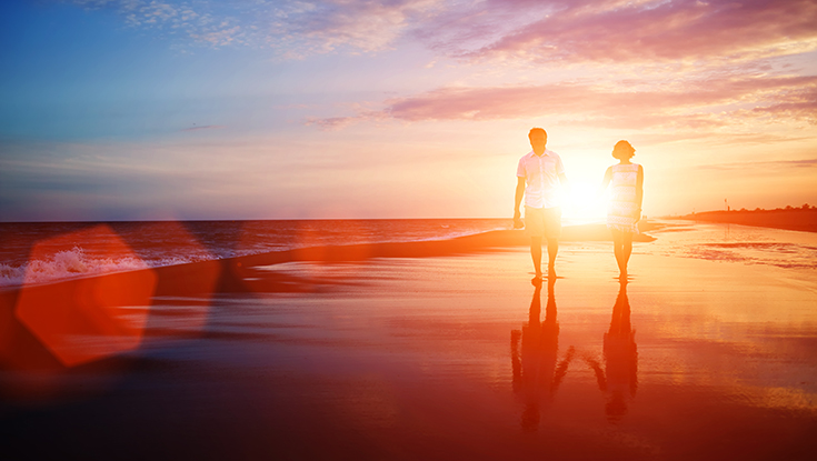 image of couple walking along sunset beach