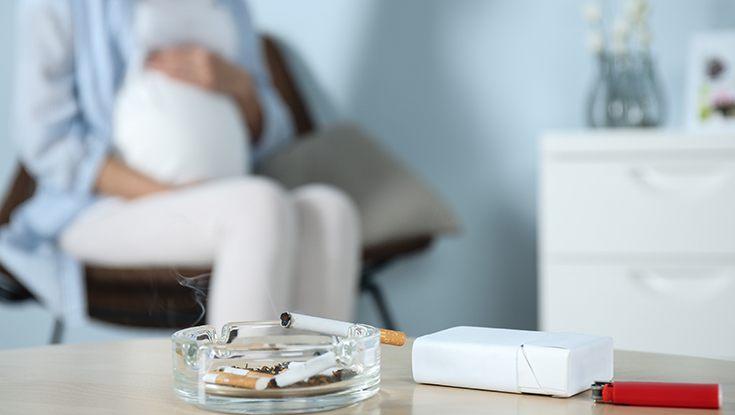 image of smoking cigarette with pregnant woman in background