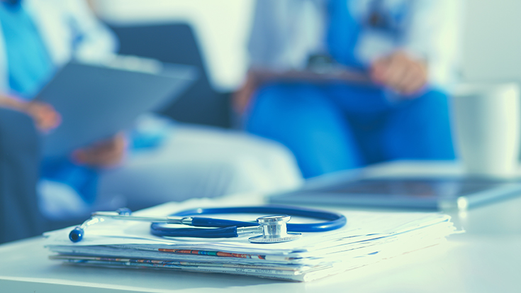 image of medical professionals engaged in a meeting with papers and stethescope in foreground