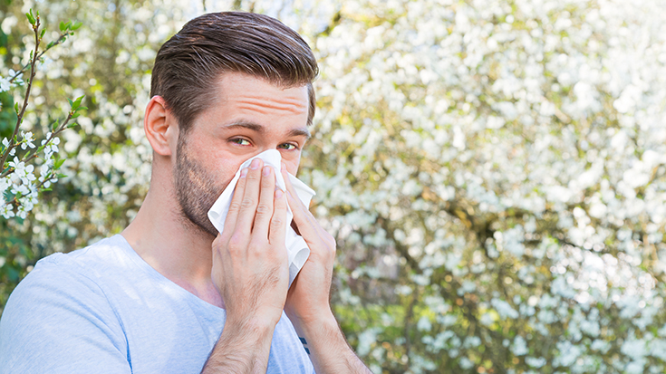 image of man outside blowing nose into tissue
