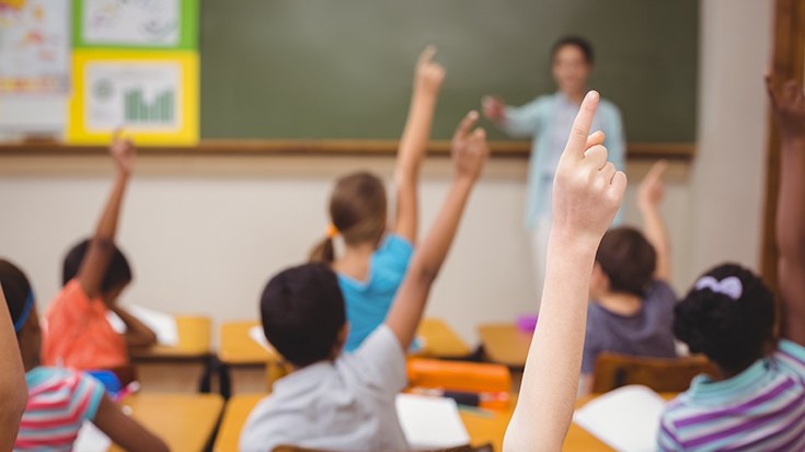 grade school kids raising their hands in classroom