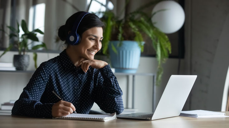 Image of woman looking at computer and taking notes